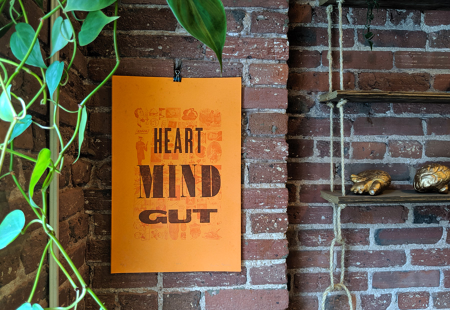 Finished letterpress print on orange paper with the inscription Heart, Mind, Gut hanging up on the wall