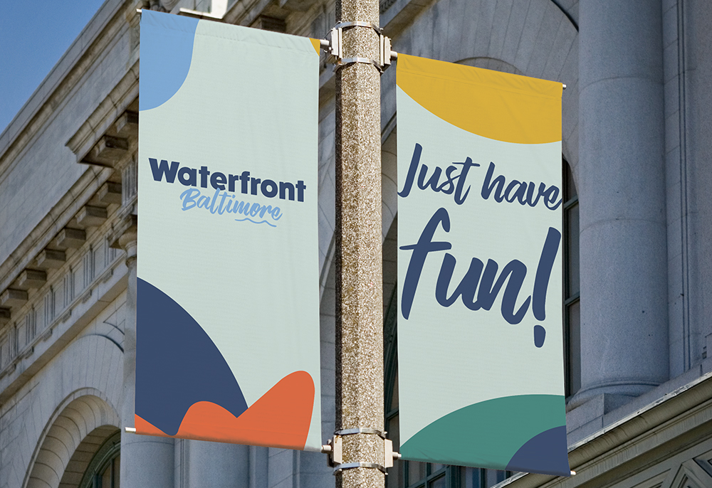 two colorful banners on a streetlamp with the imprints Waterfront Baltimore and just have fun