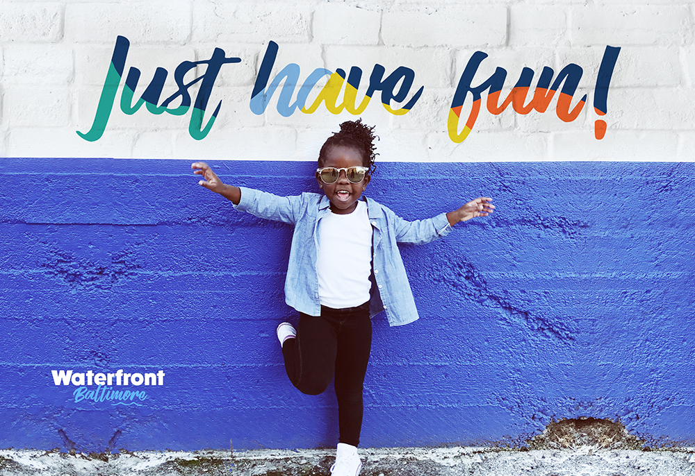 little girl with sunglasses laughing and dancing in front of a colorful wall that says just have fun