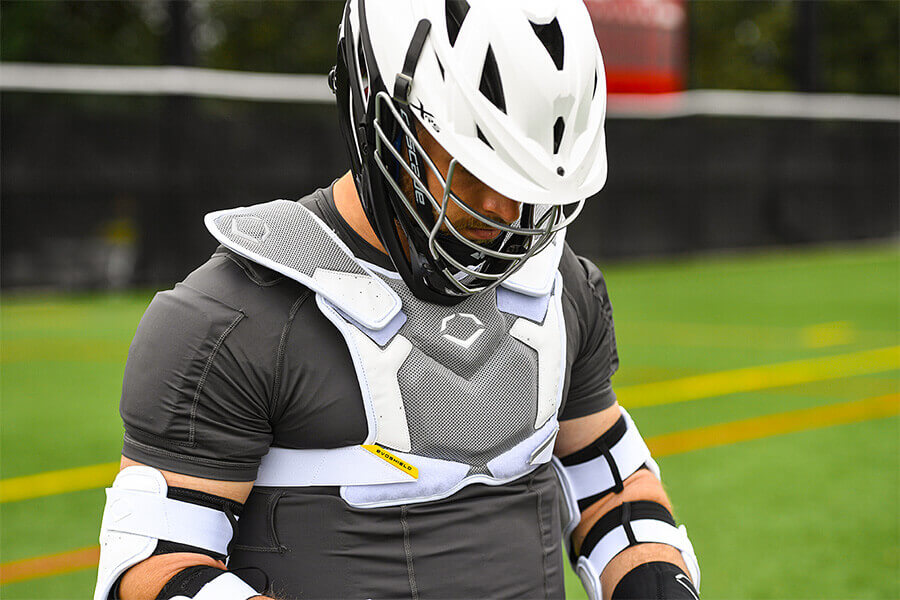 A male lacrosse player wearing a helmet, chest protector, and elbow guard.