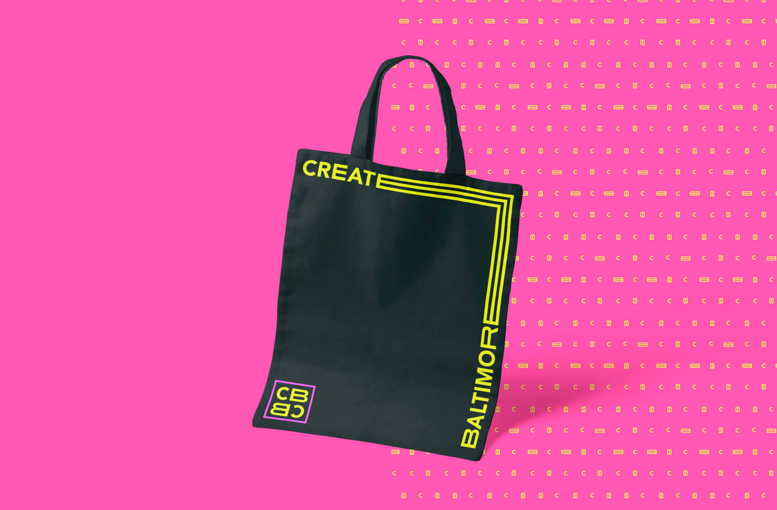 A black tote bag featuring the Create Baltimore logo and monogram in yellow text.