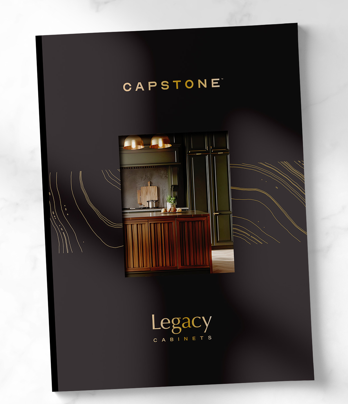 Legacy Cabinets Capstone catalog cover featuring a modern kitchen vignette framed by gold line accents on a dark background with refined typography.