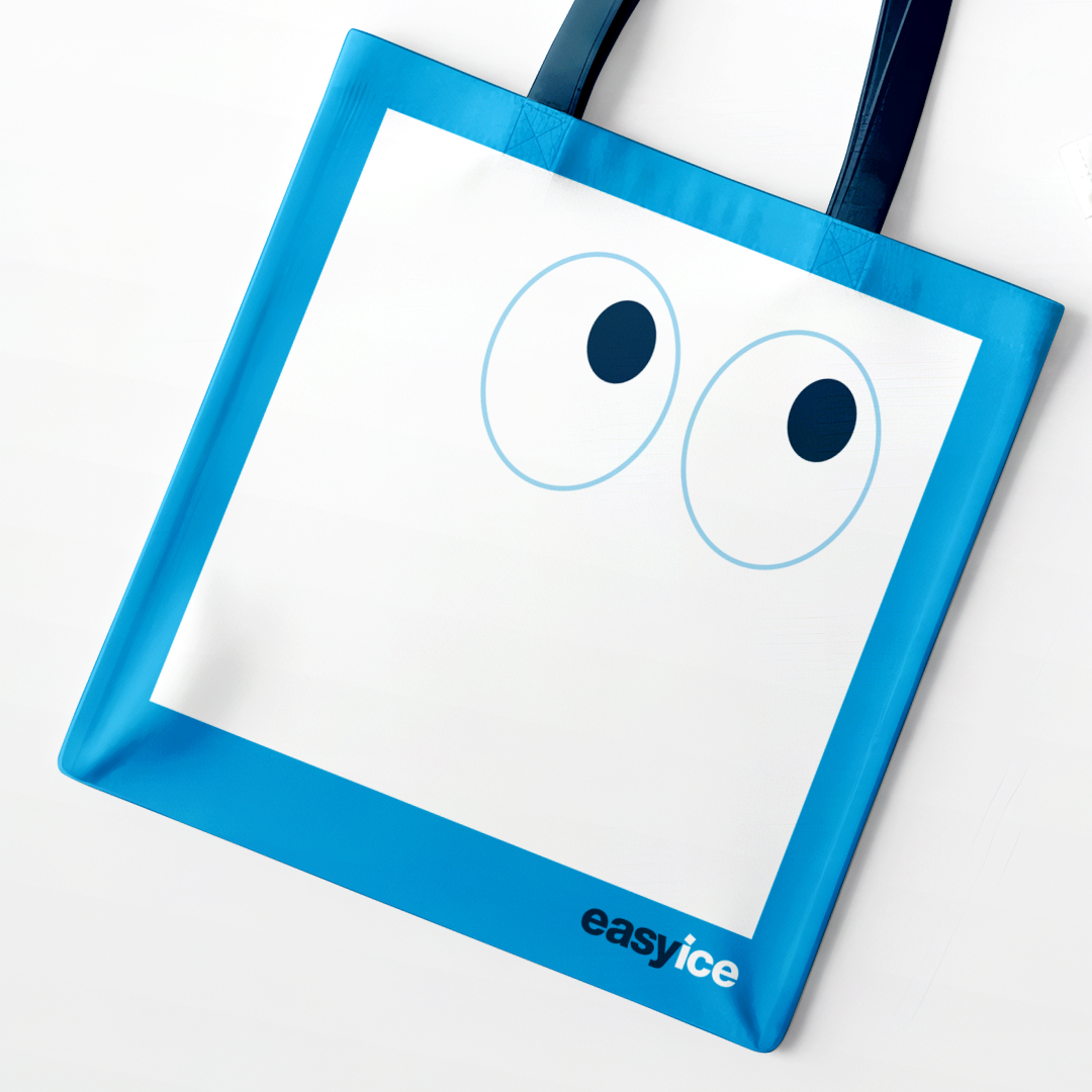 Easy Ice branded tote bag featuring a minimalist mascot-inspired face graphic with oversized eyes and a blue translucent border accented by the Easy Ice logo.